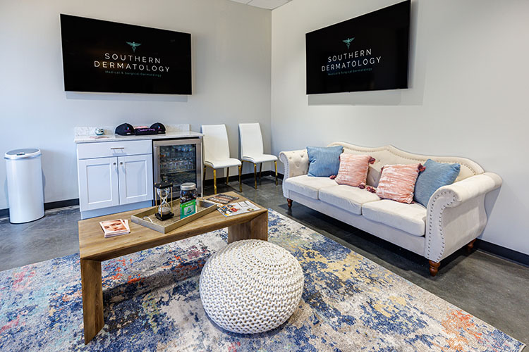 Evans waiting area — white tufted sofa, blue and coral throw pillows, navy-logo screens.